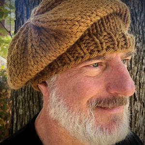 May include: A brown knitted beret with a unique folded design. The beret is worn by a person with a white beard.