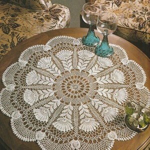 May include: A white crocheted doily with a floral design sits on a wooden table with two blue glass goblets.