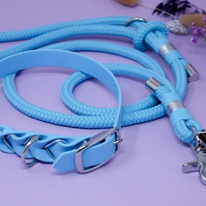 May include: A light blue dog collar and matching lead with silver hardware. The collar has a decorative braided design and the lead has a metal clip.