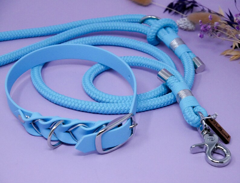 May include: A light blue dog collar and matching lead with silver hardware. The collar has a decorative braided design and the lead has a metal clip.