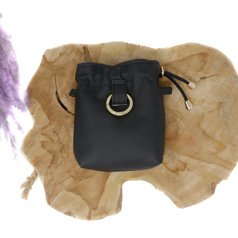 May include: Black drawstring bucket bag with a gold ring closure and a gold drawstring toggle.
