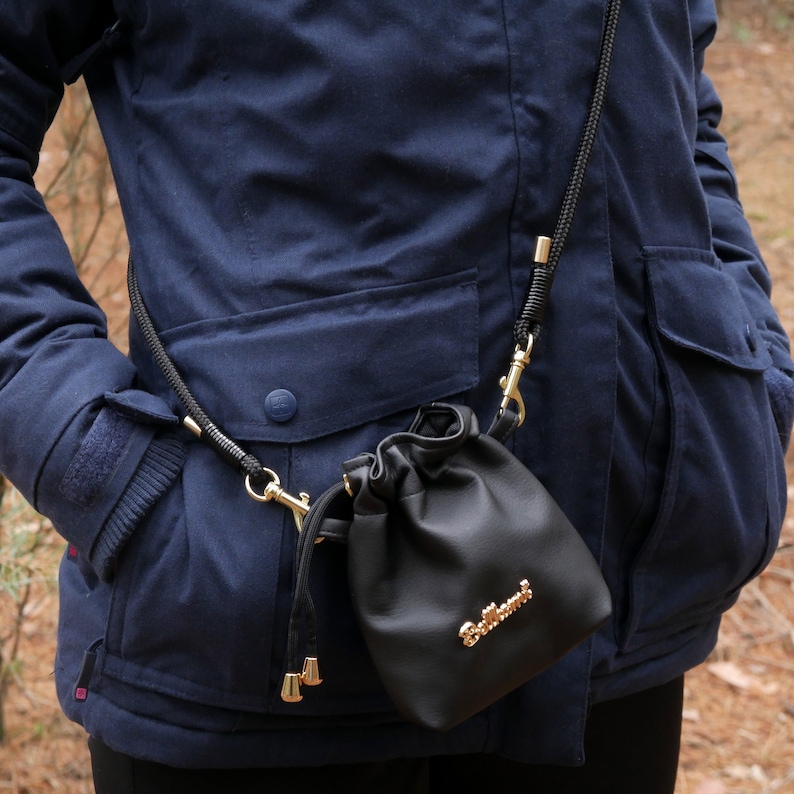 May include: A black leather drawstring bag with a gold chain strap and the word "Bellerose" embossed on the front. The bag is hanging from a person's shoulder.