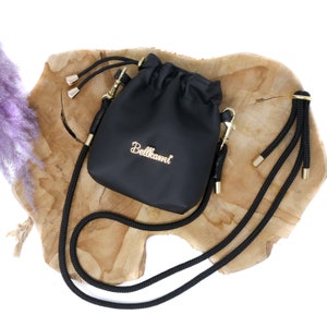May include: Black drawstring bag with a gold chain and a black rope strap. The bag has the word "Bellami" written in gold lettering.