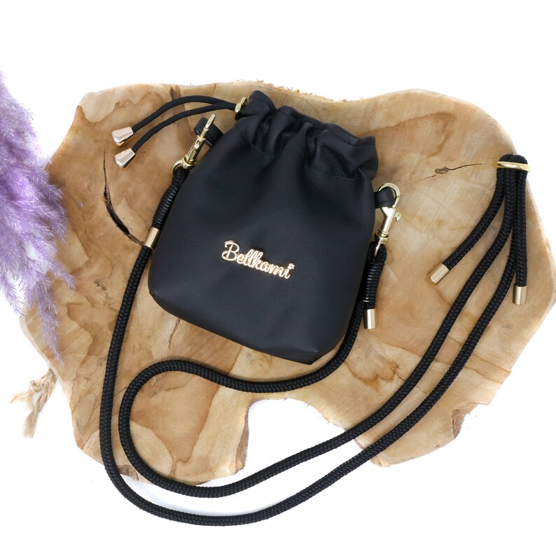 May include: Black drawstring bag with a gold chain and a black rope strap. The bag has the word "Bellami" written in gold lettering.
