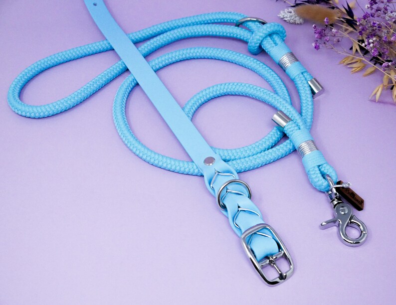 May include: A light blue leather dog collar and matching rope lead. The collar has a braided design and a silver buckle. The lead has a silver clip.
