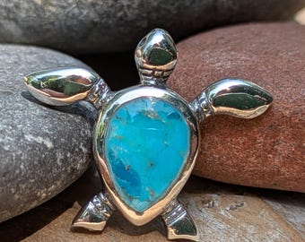 May include: A silver turtle pendant with a vibrant turquoise stone inlay. The pendant features outstretched flippers and a detailed head and legs. The turquoise stone is a bright blue color, set in a polished silver frame.