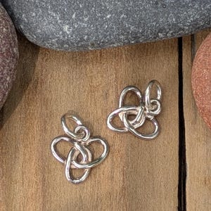 May include: Two polished silver-toned metal charms, each featuring an intricate triquetra knot design with three interconnected loops and a small circular jump ring attached to the top for hanging or connecting to a chain or bracelet.