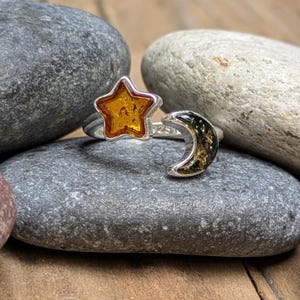 Peut inclure: Une bague ouverte en argent dotée d'une étoile à cinq branches en ambre orange translucide à une extrémité et d'un croissant de lune en ambre sombre et moucheté à l'autre, avec le poinçon 925 gravé sur l'anneau intérieur.