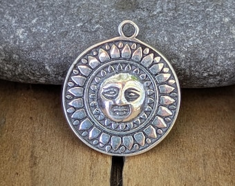 May include: A silver pendant with a sun face design. The pendant features a detailed sun face in the center, surrounded by a ring of stylized sun rays. The pendant has a loop at the top for a chain.