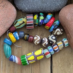 May include: A collection of assorted glass beads strung on a wire, featuring various shapes, sizes, and colors including yellow, red, blue, green, black, and white. The beads display diverse patterns such as stripes, dots, and swirls.