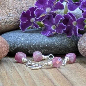 May include: A pair of earrings featuring faceted pink gemstone beads wire-wrapped in silver metal. Each earring consists of a single small pink stone attached to a silver jump ring, showcasing a simple design with metallic silver wire accents.