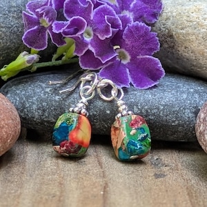 May include: A pair of dangle earrings featuring small, rectangular, multi-colored jasper beads in shades of green, blue, red, and orange. Each bead is topped with a silver-toned metal cap and attached to a silver-toned ear wire hook.