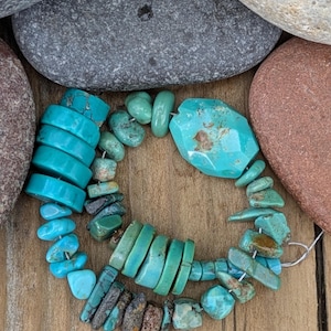 May include: A bracelet composed of various turquoise beads in shades of bright blue and green. The design features a mix of smooth, flat, cylindrical discs, irregular tumbled nuggets, and one large, faceted, polished turquoise stone.