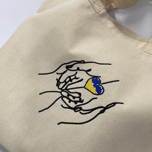 Hands holding a heart blue yellow machine embroidery