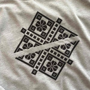 Könnte beinhalten: Ein graues Sweatshirt mit einem symmetrischen schwarzen geometrischen Design. Das Design umfasst Blumen- und Quadratmuster, die einen detaillierten, gestickten Look erzeugen. Das Sweatshirt hat einen Rundhalsausschnitt und einen lässigen Look.