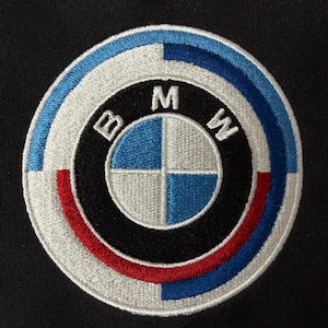 May include: Embroidered patch featuring the BMW logo. The circular emblem has a black outer ring, with the letters "B", "M", and "W" in white. The inner circle is divided into quadrants of blue and white. The outer ring has blue, red, and white accents.