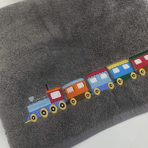 Puede incluir: Una toalla gris con un diseño bordado de un tren de colores. El tren tiene varios vagones y ruedas. La toalla tiene el texto "PALOMA - ЦЕНТР ПРОФЕССИОНАЛЬНОЙ ВЫШИВКИ" en la esquina superior izquierda.