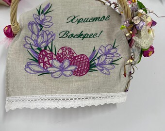 May include: A white linen Easter basket with a green embroidered message that says "Happy Easter!" in Russian. The basket is decorated with purple flowers and pink eggs.