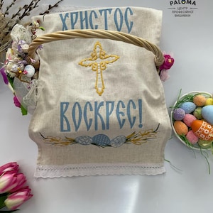 May include: A white linen Easter basket liner with blue and gold embroidery. The liner features the text "Христос Воскрес!" (Christ is Risen!) and a cross. The liner has a white lace trim.