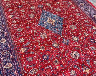 May include: A red and blue Persian rug with a floral pattern. The rug has a dark blue border with intricate designs.