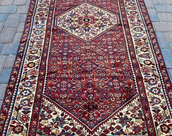 May include: A vintage Persian rug with a red background and intricate floral patterns in shades of blue, cream, and red. The rug has a central diamond shape with a floral design and a border with a repeating floral motif.