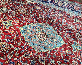 May include: A red, blue, and cream colored Persian rug with a floral pattern. The rug has a central medallion with a blue background and a cream colored floral design.