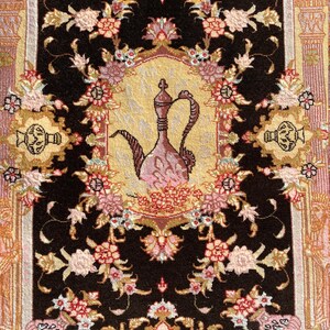 Può includere: Un tappeto nero con un motivo floreale e un design oro e rosa al centro. Il design presenta una brocca stilizzata con un beccuccio e un manico.