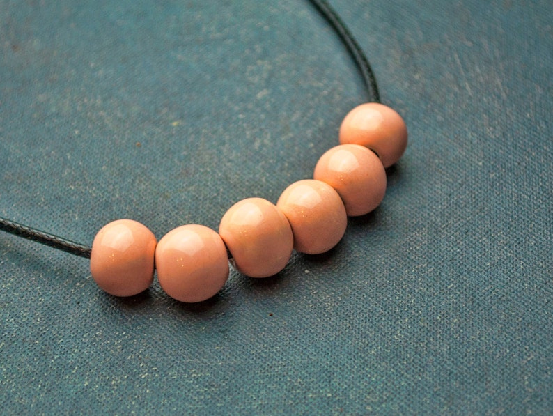 May include: A necklace with a black cord and six peach-coloured wooden beads.