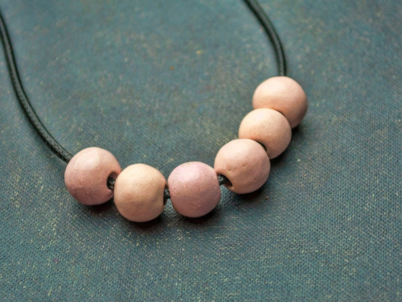 May include: A necklace with a black cord and six pink ceramic beads.