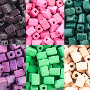 Può includere: Assortimento di perline di legno quadrate in vari colori, tra cui viola, rosa, verde, verde acqua e beige. Le perline hanno una superficie ruvida e testurizzata.
