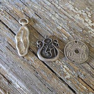 Può includere: Tre ciondoli d'argento, uno a forma di orologio da tasca, uno con un designo di viso e uno rotondo con il testo "10 10" e "10 CENTI" su di esso.