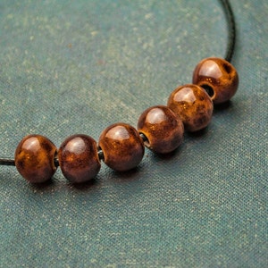 May include: A brown and black beaded necklace with a black cord. The beads are round and have a speckled pattern.