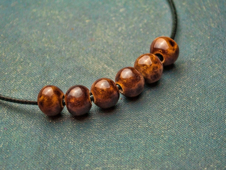May include: A brown and black beaded necklace with a black cord. The beads are round and have a speckled pattern.