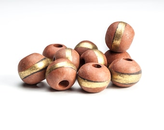 May include: A group of brown ceramic beads with gold accents. The beads are round and have a hole in the centre. They are arranged in a pile on a white background.