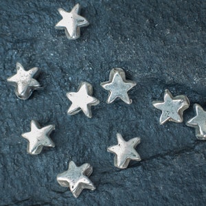 May include: Nine silver star-shaped beads on a dark grey background.