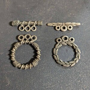 May include: Four silver-toned metal clasps for jewelry making. Two are round with a twisted rope design, one is a simple bar with three rings, and the other is a leaf design with three rings.