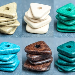 Könnte beinhalten: Ein Satz von fünf dreieckigen Perlen in verschiedenen Farben, darunter Beige, Weiß, Grün, Blau und Braun. Die Perlen haben ein Loch in der Mitte und sind übereinander gestapelt.