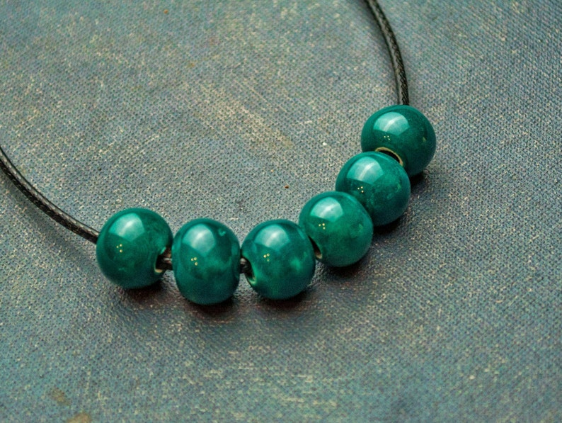 May include: A necklace with six teal green beads strung on a black cord.