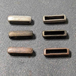 May include: Six metal rectangular buckles in different finishes: silver, brass, black, copper, and bronze. The buckles are all the same size and shape.