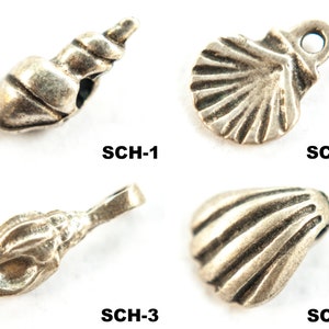 Könnte beinhalten: Vier silberfarbene Metall-Anhänger in Form von Muscheln und einer Muschel. Die Anhänger sind mit SCH-1, SCH-2, SCH-3 und SCH-4 beschriftet.