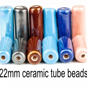 Könnte beinhalten: Ein Satz von 22 mm Keramik-Röhrenperlen in verschiedenen Farben, darunter Blau, Grau, Braun und Rosa. Die Perlen sind in einer Reihe angeordnet, wobei die Enden der Perlen sichtbar sind.
