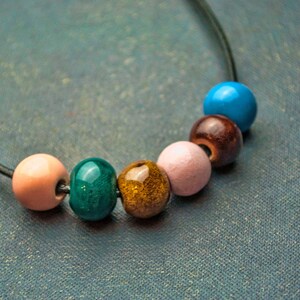 May include: A necklace with six colourful beads, including pink, green, brown, blue, and gold. The beads are strung on a black cord.