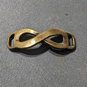 Peut inclure: Un charme en métal doré en forme de symbole d'infini avec deux boucles. Le charme a une finition lisse et polie.