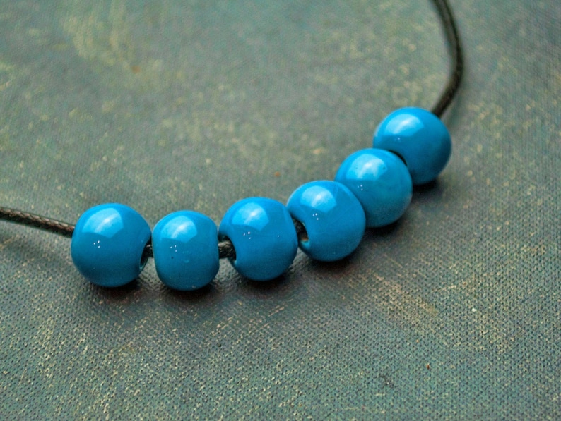 May include: A necklace with six bright blue beads strung on a black cord.