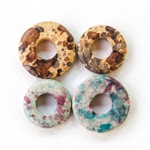 Peut inclure: Quatre perles en céramique rondes en forme de beigne avec un trou au centre. Les perles sont décorées d'éclaboussures de peinture brune, blanche et bleue.