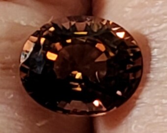 May include: A faceted, round gemstone with a dark brown hue. The gem's surface reflects light, creating highlights and shadows. The cut reveals multiple facets, enhancing its brilliance. The gemstone is likely a jewelry component.