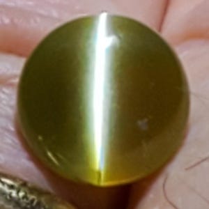 May include: A round, green gemstone with a shimmering, iridescent effect. The stone has a smooth, polished surface.