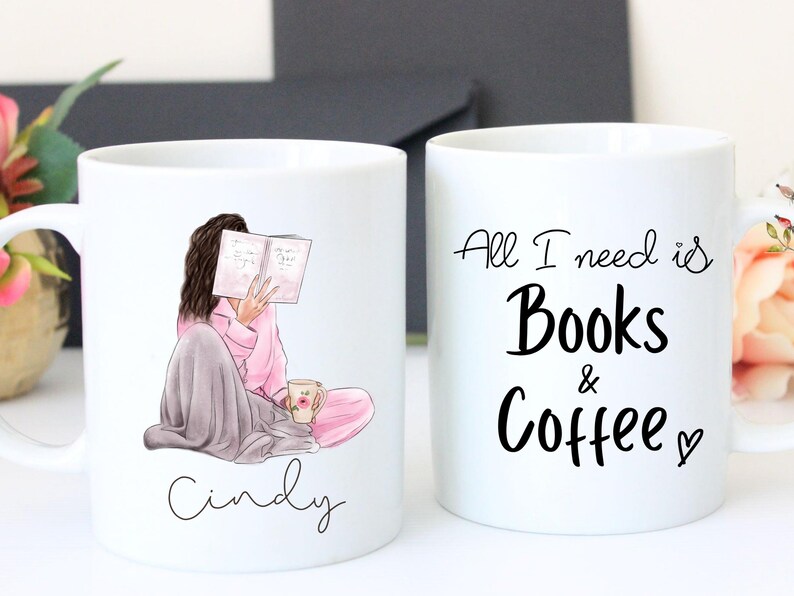 May include: Two white ceramic mugs. One mug features an illustration of a person reading a book, wrapped in a blanket, with the name "Cindy" below. The other mug has the text "All I need is Books & Coffee".