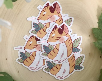 May include: Three cute cartoon tiger stickers with orange and white stripes, surrounded by green leaves. The stickers are on a wooden surface.