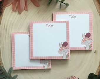 May include: Three pink gridded notepads with the word "Notes" printed on each. Each notepad features a snail on a mushroom illustration.